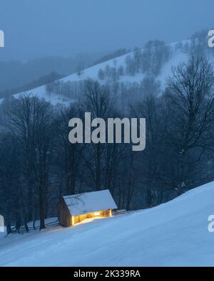 Abenddämmerung Blick auf eine einsame Hütte in einem verschneiten Bergwald im Winter Stockfoto