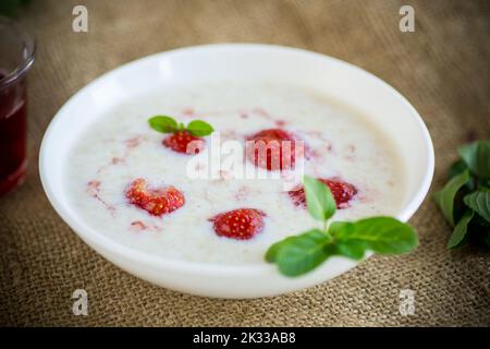 Süßer Haferflocken mit Erdbeeren auf einem Teller, auf einem Holztisch. Stockfoto