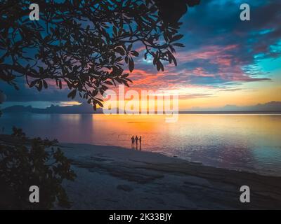 Menschen beobachten den farbenfrohen Sonnenuntergang am tropischen Strand. Rosa, blaue, orangefarbene Farben spiegeln sich im Meerwasser wider. Erstaunlicher natürlicher Hintergrund. Wunderschöne Naturlandschaft. Reisen, Tourismus, Abenteuer, Konzept. Stockfoto