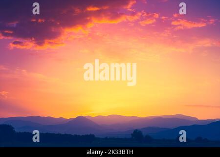 Schöne Bergkette mit Sonnenuntergangssonne in orangefarbenem Himmel mit bunten Wolken. Atemberaubende Naturkulisse. Natürliche Textur und Hintergrund Stockfoto