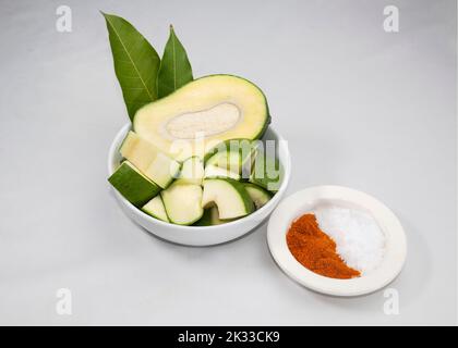 Eine Schüssel mit rohen grünen Mangos mit Pfeffer und Salz isoliert auf weißem Hintergrund. Stockfoto