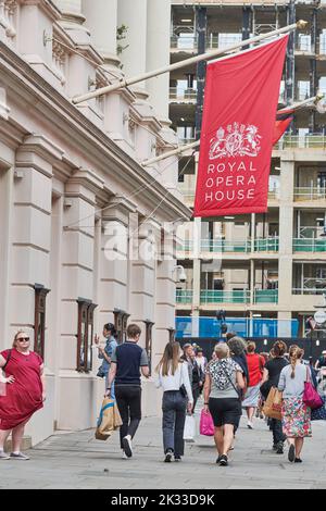 Vor dem Haupteingang des Royal Opera House (Roh), Bow Street, London, England, passieren die Käufer unter der Flagge Stockfoto