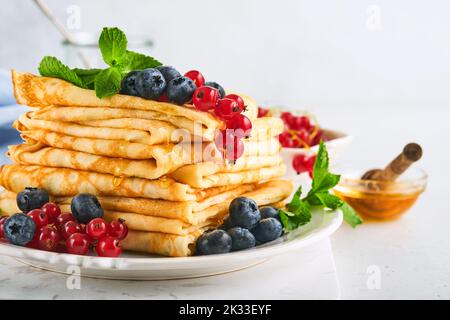 Pfannkuchen. Stapel von Crepes oder dünnen Pfannkuchen mit Beeren, Heidelbeeren, roten Johannisbeeren, Himbeeren und Honig zum Frühstück. Hausgemachtes Frühstück. Kopieren Sie den SPAC Stockfoto