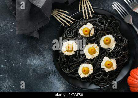 Halloween Party italienische schwarze Pasta dekoriert Horror Oliven wie Augen auf schwarzem Teller auf alten dunklen Tisch Hintergrund. Monster Gesicht von Pasta. Halloween Stockfoto
