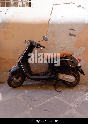 Schwarze Vespa und eine beige Mauer in der Stadt Lucca, Toskana, Italien Stockfoto