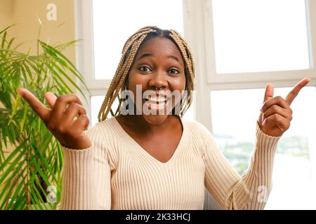 Afroamerikanische Frau, die im Wohnzimmer und zu Hause lacht und eine lustige Geschichte erzählt Stockfoto