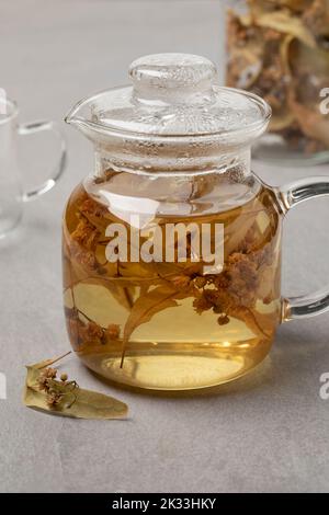 Glas-Teekane mit getrockneter tilia-Blüte aus nächster Nähe und getrockneter Blüte davor Stockfoto