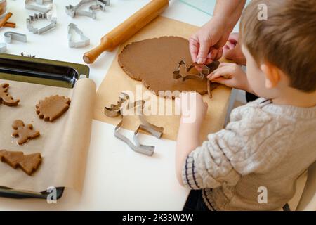 Der Junge schneidet aus dem Teig einen weihnachtlichen Lebkuchenmann in Form eines Hirsches Stockfoto