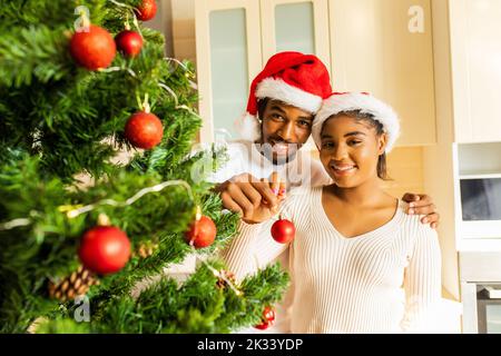 lateinisches hispanische Paar, das zu Hause einen weihnachtsbaum mit roter Kugel schmückt Stockfoto