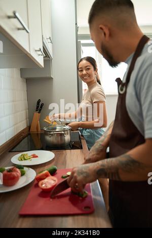 Mann schneidet Gemüse und kommuniziert mit seiner Frau in der Küche Stockfoto