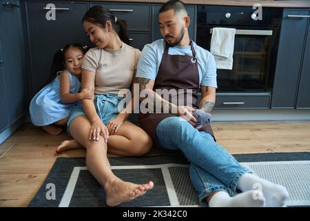 Mädchen mit asiatischen Eltern bequem in der Küche auf dem Boden eingebettet Stockfoto