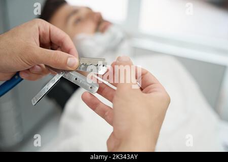 Vorsichtiger Barbier, der sich bereit gemacht hat, das Gesicht der Gäste mit einem Rasiermesser zu rasieren Stockfoto