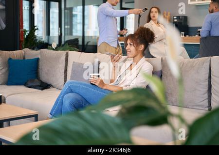 Fröhliche Dame mit Smartphone-Gespräch im Co-Working-Raum Stockfoto