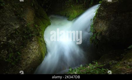 Detail eines kleinen Wasserfalls in Charco Pataco mit kristallklarem Wasser zwischen Felsen mit schwacher Beleuchtung in Letur, Albacete, Spanien Stockfoto