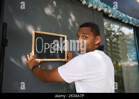 Ein Mann hängt ein Schild an die Wand des Ladens Stockfoto