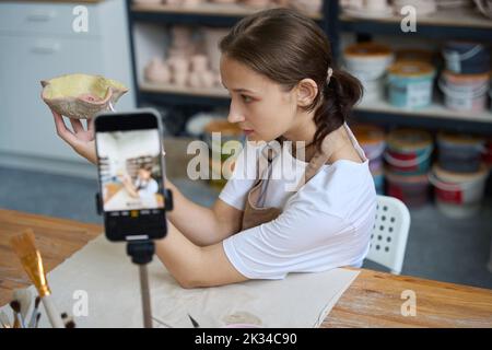 Die Schülerin hält einen dekorativen Teller in den Händen und macht ein Selfie Stockfoto