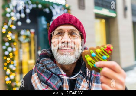 Glücklicher Mann zeigt grüne süße Cookie weihnachtsbaum Form im Freien im Wintermarkt Stockfoto