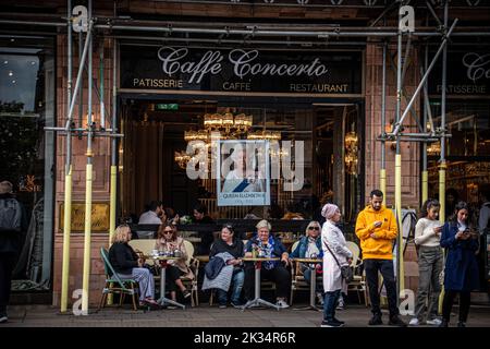 Leute saßen vor einem Café mit einem Poster der Königin im Fenster Stockfoto