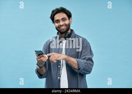 Glücklicher arabischer Mann Student mit Handy isoliert auf blauem Hintergrund. Stockfoto