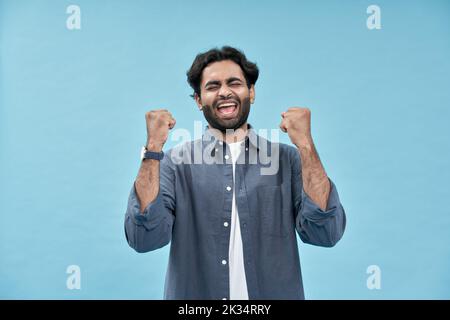 Glücklich aufgeregt arabischen jungen Mann Heben Fäuste isoliert auf blauem Hintergrund. Stockfoto