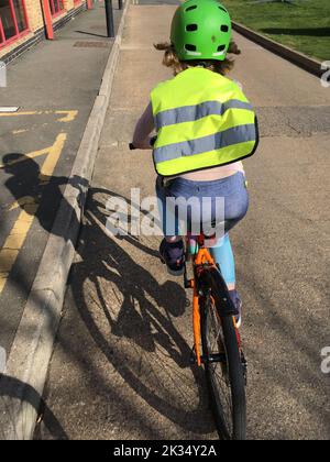 Eine siebenjährige Fahrradfahrerin Pedale ihr Fahrrad / fährt sicher mit hoher Sichtbarkeit / hallo vis Kleidung und einem Fahrradhelm, während sie ihr Fahrrad an einem sonnigen Tag reitet. VEREINIGTES KÖNIGREICH (132) Stockfoto