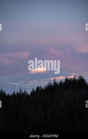 Wunderschöne Alpen Glow treffen Berggipfel in den schottischen Highlands während des atemberaubenden Sonnenaufgangs in der Winterlandschaft Stockfoto