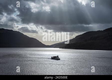 Atemberaubende majestätische Sonnenstrahlen, die während des Sonnenuntergangs im Winter durch dramatische Wolken auf das ruhige Wasser der Landschaft von Loch Lomond strömen Stockfoto