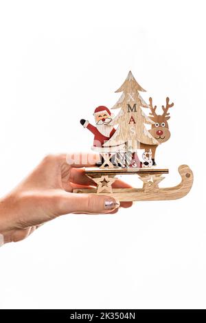 Ein vertikales Bild einer Hand, die eine hölzerne Weihnachtsdekoration mit einem Weihnachtsmann und Hirsch zeigt Stockfoto
