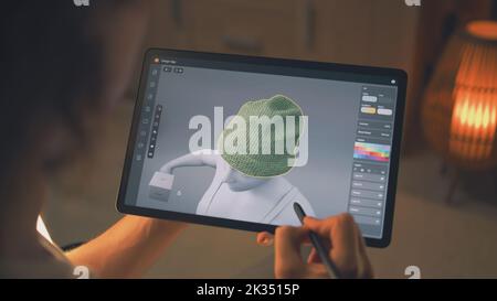 Junger männlicher 3D-er Designer, der aus der Ferne an 3D Visualisierungen von Kleidung in der Design-App mit digitalem Tablet-Computer und Stylus arbeitet Stockfoto