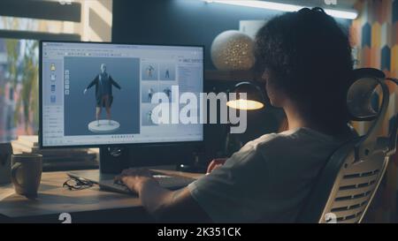 Männlicher junger 3D-Designer, der Remote-Arbeit an 3D Modellierung und Gestaltung von Kleidung mit pc mit professioneller Software hat, während er zu Hause am Tisch sitzt Stockfoto
