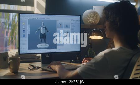 Männlicher junger 3D-Designer, der Remote-Arbeit an 3D Modellierung und Gestaltung von Kleidung mit pc mit professioneller Software hat, während er zu Hause am Tisch sitzt Stockfoto