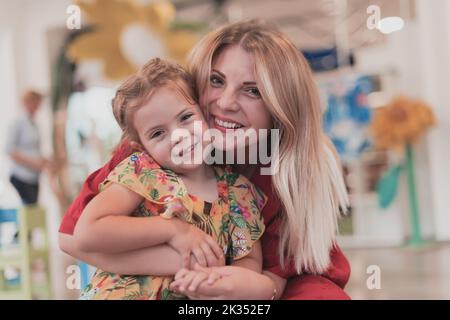 Ein niedliches kleines Mädchen küsst und umarmt ihre Mutter im Kindergarten Stockfoto