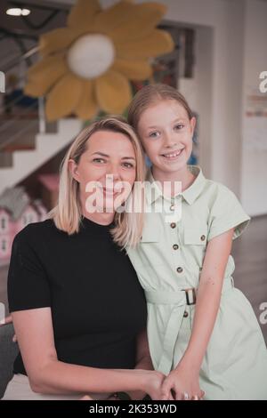 Ein niedliches kleines Mädchen küsst und umarmt ihre Mutter im Kindergarten Stockfoto