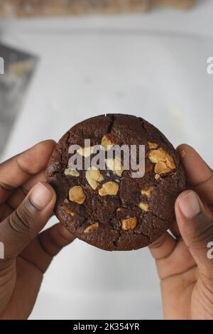 Draufsicht auf Hand mit dreifachem Schokoladenkeksen, flacher Laie von dunklem Schokoladenkekie, Schokoladenkekie in weiblichen Händen Stockfoto