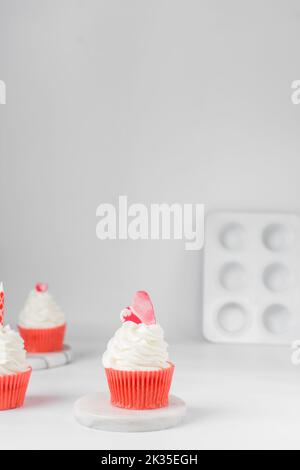 Weißer und roter Cupcake mit Herz auf weißem Hintergrund, weißer Milchschaum auf einem roten Cupcake, Tagestörte am Valentinstag, Dessert zum valentinstag Stockfoto