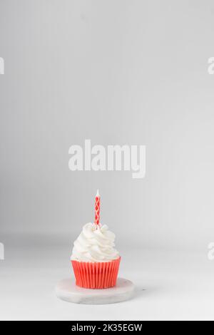 Weißer und roter Cupcake mit einer Kerze oben, weißer Zuckerguss auf einem roten Cupcake, Tagestörtchen am Valentinstag Stockfoto