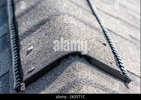 Auf einem Schindeldach installierter Lüftungsschlitz mit Kappendeckel zur passiven Dachbodenlüftung in einem Wohnhaus. Stockfoto