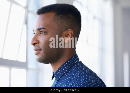 Über seine Zukunft nachdenken. Profil eines jungen ethnischen Mannes, der nachdenklich aus einem Fenster schaut. Stockfoto