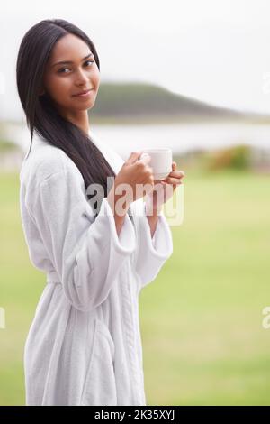 Die Ruhe des Augenblicks genießen. Eine schöne junge Frau genießt eine Tasse Kaffee, während sie einen Bademantel trägt. Stockfoto