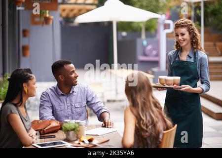 Was kann ich noch bekommen? Eine Kellnerin, die ihre Kunden in einem Café bedient. Stockfoto