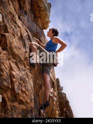 Sie brauchen Ausdauer, um eine Felskletterin zu sein. Eine junge Frau, die eine Felswand bestieckt. Stockfoto