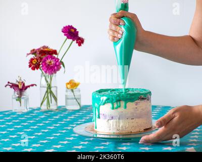 Frau, die das Sahnehäubchen verteilt, um die Oberseite des Kuchens zu bedecken. Hausgemachtes Backen, handgefertigt. Freie Zeit in Quarantäne. Konditorhands, die einen Kuchen mit Minze Fi überbacken Stockfoto