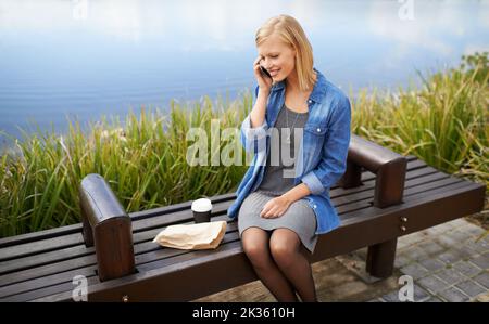 Treffen mit Freunden während meiner Mittagspause. Eine attraktive Frau, die während ihrer Mittagspause im Park telefoniert. Stockfoto