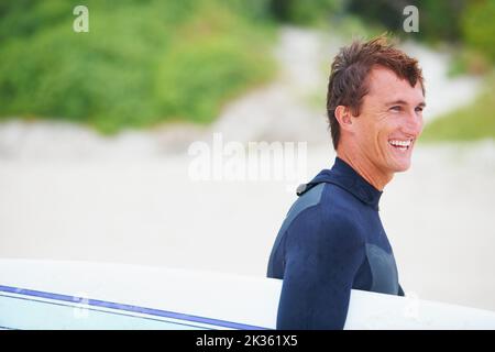 Raus auf die Wellen. Ein junger Surfer, der sein Brett am Strand trägt. Stockfoto