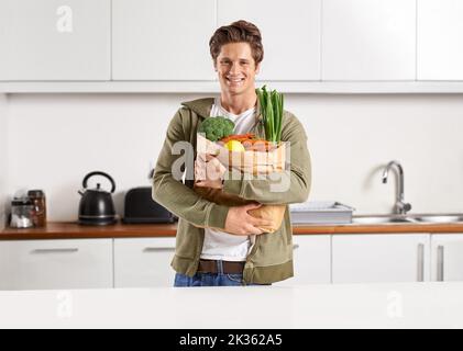 Frisch vom Markt. Ein junger Mann in einer Küche, der einen braunen Papierbeutel mit Gemüse hält. Stockfoto