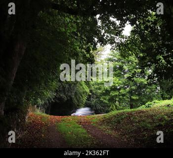 Am oberen Ende des Westjordanlands, in Winster in Derbyshire, kommt an einem langweiligen Tag ein Auto um die Ecke, während die Scheinwerfer eingeschaltet sind und weiße Lichtspuren verursachen Stockfoto