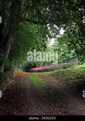 Am oberen Ende des Westjordanlands, in Winster, fährt an einem langweiligen Tag ein Auto um die Ecke, wobei die Bremsleuchten eine rote Kurve von hellen Wegen verursachen Stockfoto