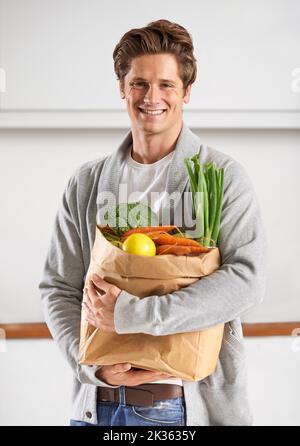 Nur Bio für mich. Ein junger Mann in einer Küche, der einen braunen Papierbeutel mit Gemüse hält. Stockfoto