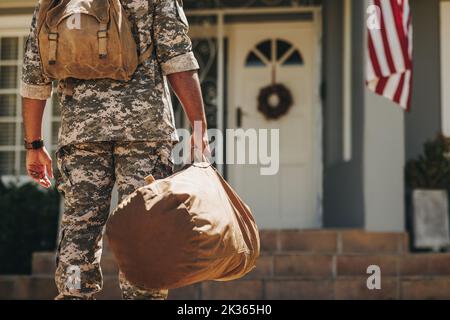 Nicht erkennbarer Soldat, der mit seinem Gepäck vor seinem Haus steht. Rückansicht eines patriotischen amerikanischen Militäranmannes, der nach seiner Verdienung nach Hause kam Stockfoto