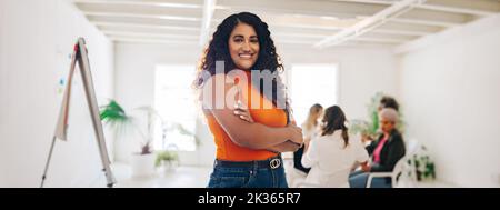 Fröhliche junge Geschäftsfrau, die in einem kreativen Büro vor der Kamera lächelt. Fröhliche junge Geschäftsfrau, die an einem Treffen mit ihrem Kollegen teilnimmt Stockfoto